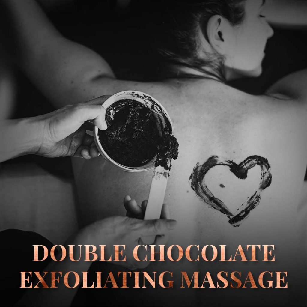 A smiling woman lays on her stomach while a heart is spread on her back with chocolate massage oils.